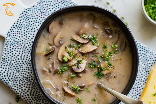 عکسی از یک کاسه مشکی رنگ که درون آن سوپ قارچ و خامه ریخته شده است و یک قاشق در آن است.