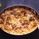 عکسی از یک ظرف غذا است. دورن آن گراتن مرغ و سیب زمینی و قارچ قرار دارد. سمت راست این ظرف یک قاشق غذا است که در گراتن مرغ فرو رفته است.
