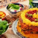 عکسی از یک سفره تزیین شده به همراه ته چین گوجه فرنگی با مرغ و قارچ که روی ته چین با زعفران و زرشک تزیین شده و در کنار ظرف ته چین ظرف سبزی، کاسه ترشی، کاسه ماست و یک لیوان دوغ قرار دارد.